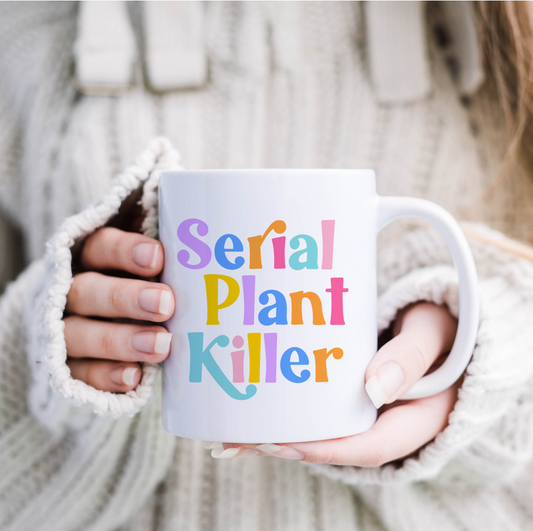 "Person holding 'Serial Plant Killer' mug, playful rainbow text on white. A sip of humor and charm!"