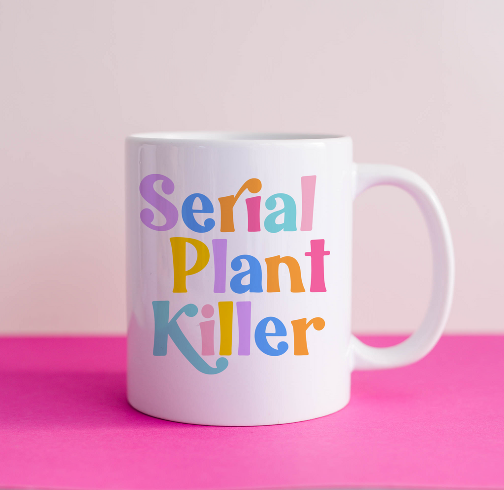 "Studio shot of 'Serial Plant Killer' mug against pink backdrop. Vibrant design with rainbow-colored text."