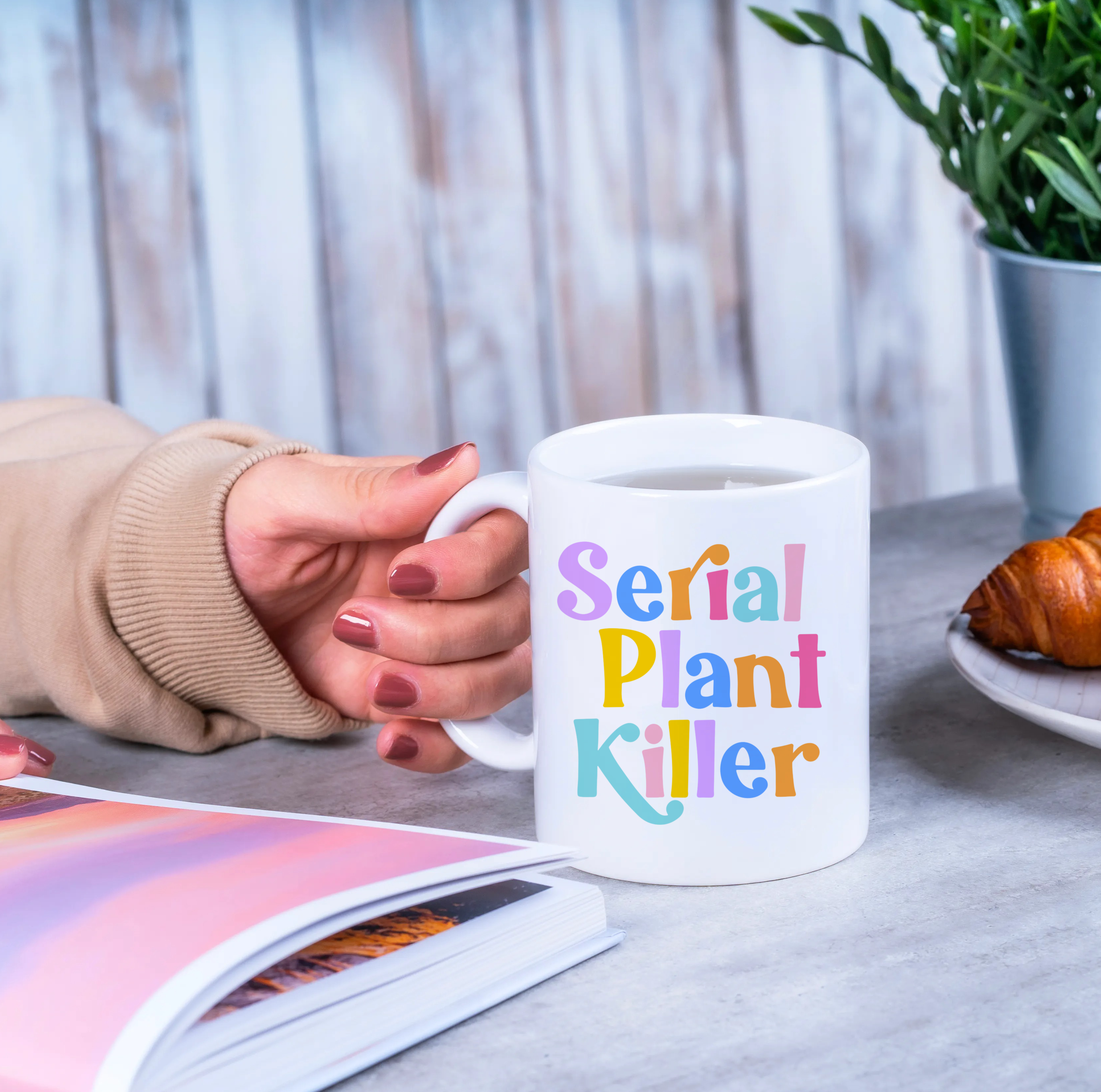 "Far away view of person holding 'Serial Plant Killer' mug. Rainbow text adds a pop of color to your morning!"