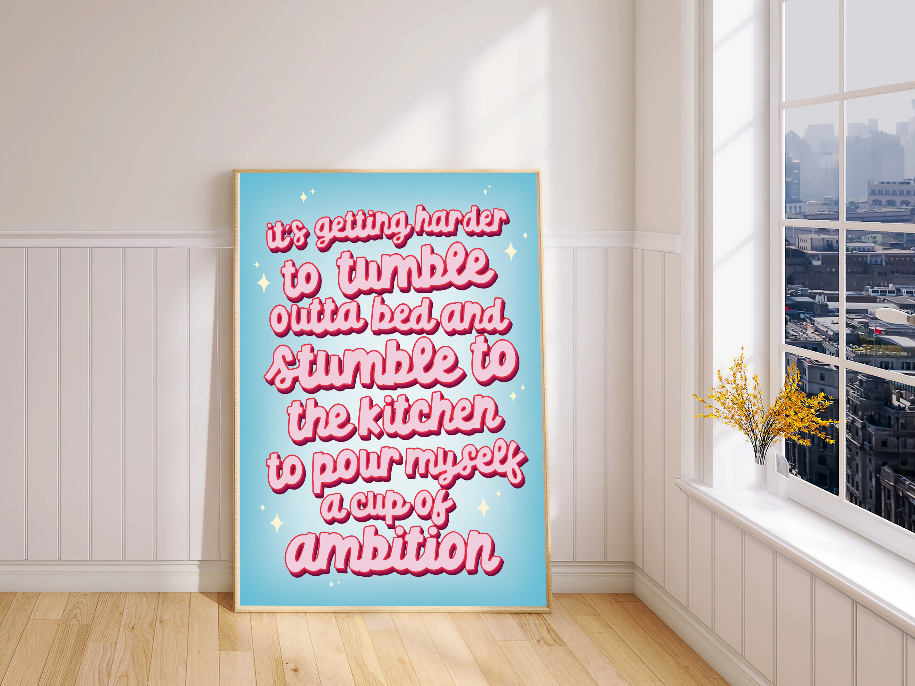 "Framed print: 'It's Getting Harder to Tumble Out of Bed and Stumble to the Kitchen, to Pour Myself a Cup of Ambition.' Playful blue backdrop, pink cursive typography."